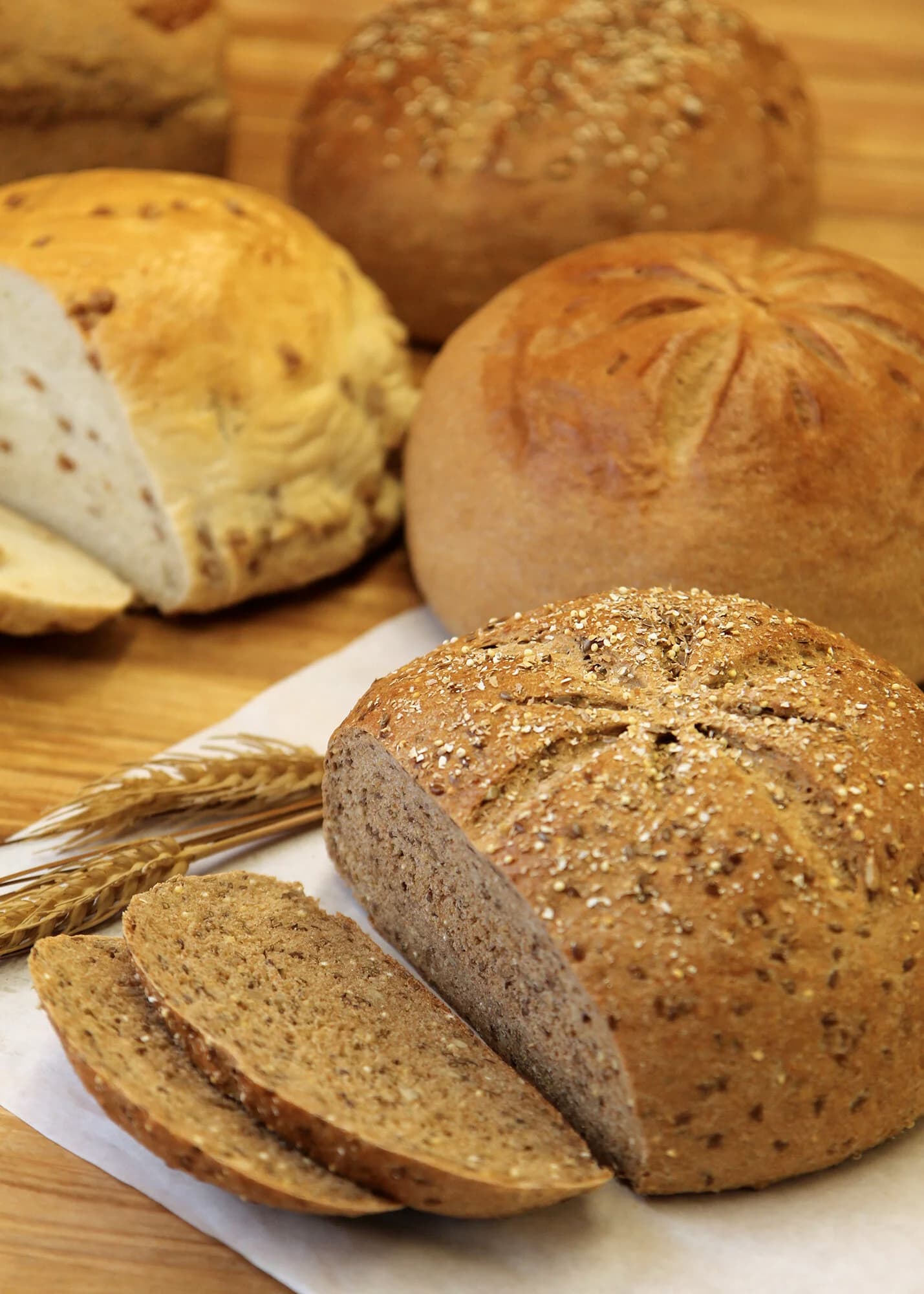 Fresh-baked round loaves on a wooden board, one sliced to show its seeded whole grain crumb